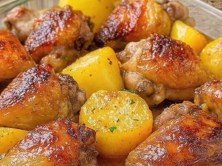 A golden, crispy chicken thigh and roasted potato wedge in a glass dish with herb garnish.