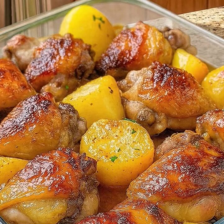 A golden, crispy chicken thigh and roasted potato wedge in a glass dish with herb garnish.