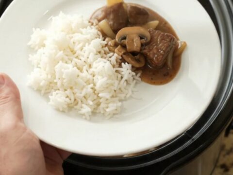 Bourbon gravy mushroom ribeye bites in a slow cooker, with a spoon lifting a bite.