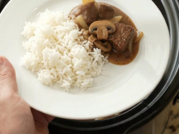 Bourbon gravy mushroom ribeye bites in a slow cooker, with a spoon lifting a bite.