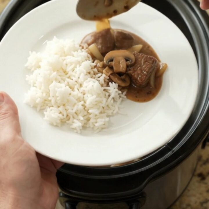 Bourbon gravy mushroom ribeye bites in a slow cooker, with a spoon lifting a bite.
