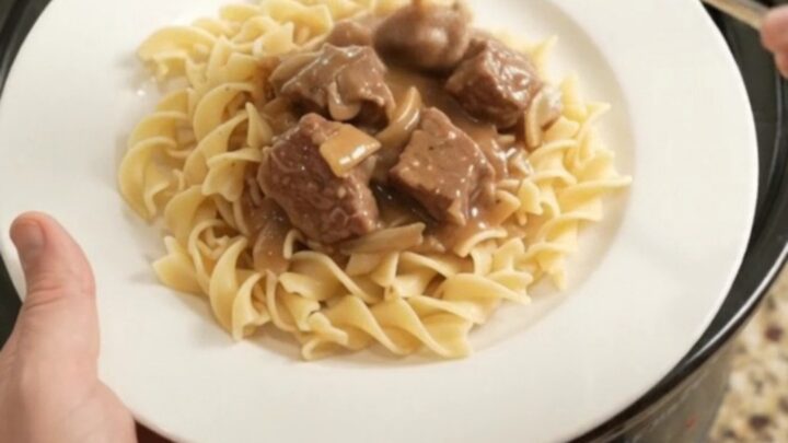 Slow cooker ribeye bites in creamy mushroom gravy with onions, served over buttered noodles