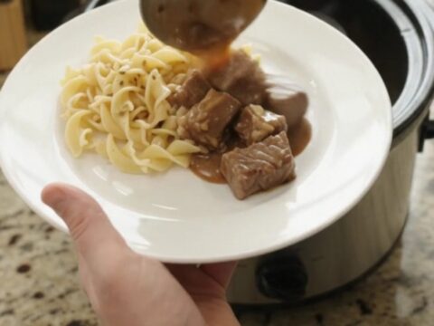 Slow cooker full of ribeye bites and baby potatoes in rich brown gravy, with steam rising