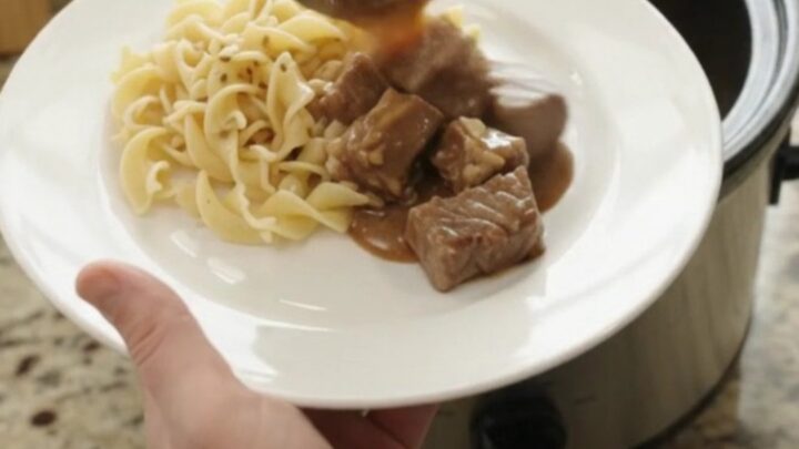Slow cooker full of ribeye bites and baby potatoes in rich brown gravy, with steam rising