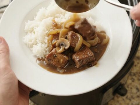 Slow cooker full of ribeye bites and caramelized onions in rich bourbon gravy