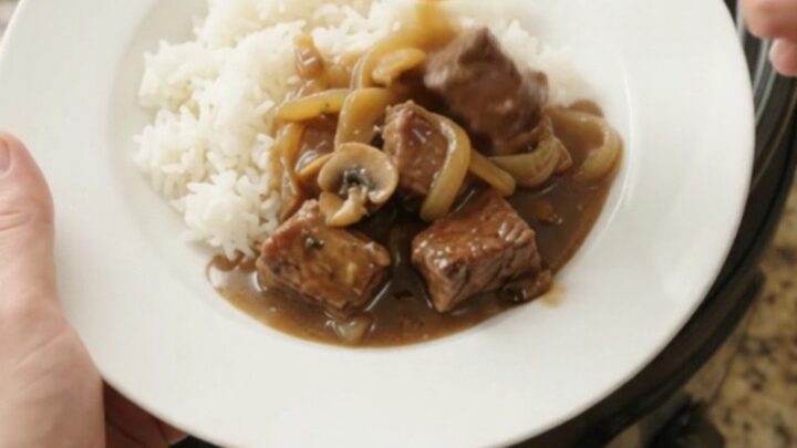 Slow cooker full of ribeye bites and caramelized onions in rich bourbon gravy