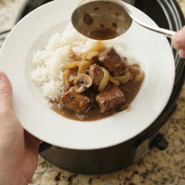 Slow cooker full of ribeye bites and caramelized onions in rich bourbon gravy