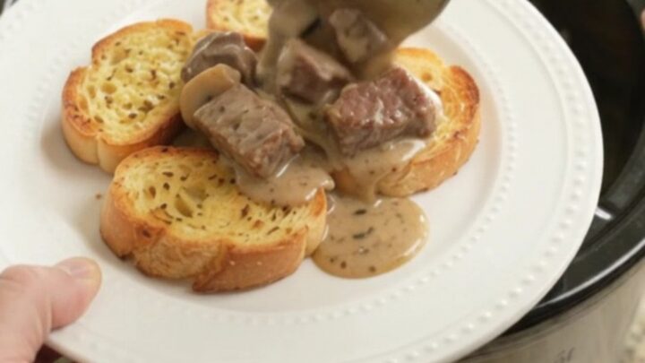 A slow cooker filled with creamy ribeye bites, broccoli, and mushrooms in a Gruyère sauce.