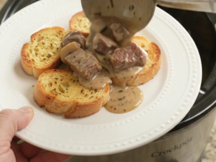A slow cooker filled with creamy ribeye bites, broccoli, and mushrooms in a Gruyère sauce.