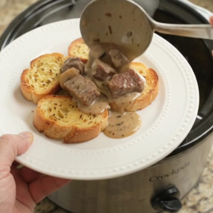 A slow cooker filled with creamy ribeye bites, broccoli, and mushrooms in a Gruyère sauce.
