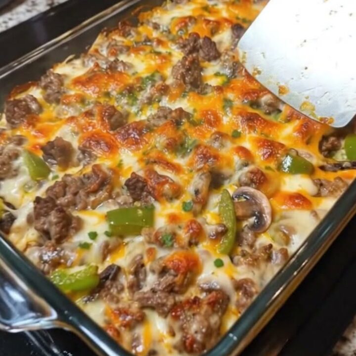 A glass baking dish filled with a cheesy Philly cheesesteak casserole, showing melted cheese and beef.