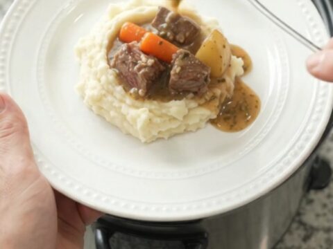 Slow-cooker ribeye bites with carrots and potatoes in a rich butter au jus, served in a black crockpot.