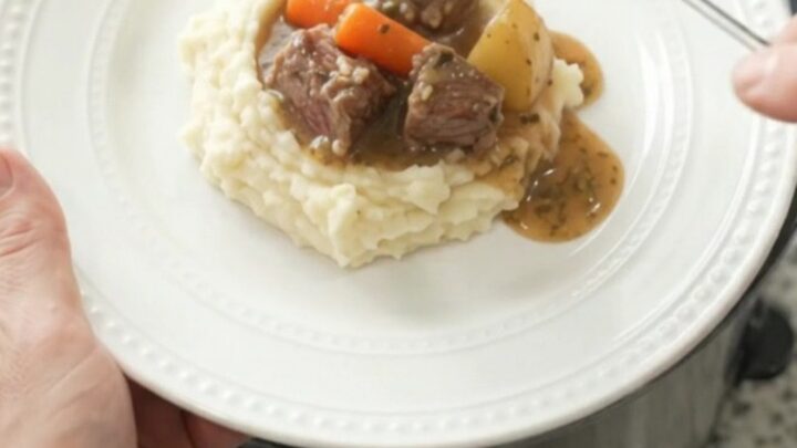 Slow-cooker ribeye bites with carrots and potatoes in a rich butter au jus, served in a black crockpot.