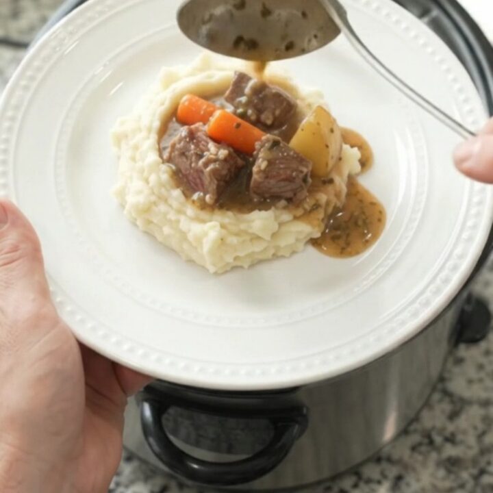 Slow-cooker ribeye bites with carrots and potatoes in a rich butter au jus, served in a black crockpot.