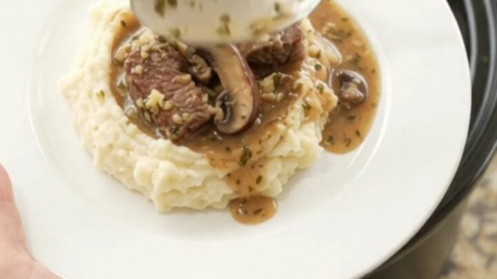 Slow cooker ribeye bites and portobello mushrooms in a rich garlic-herb butter au jus, served in a black crockpot.