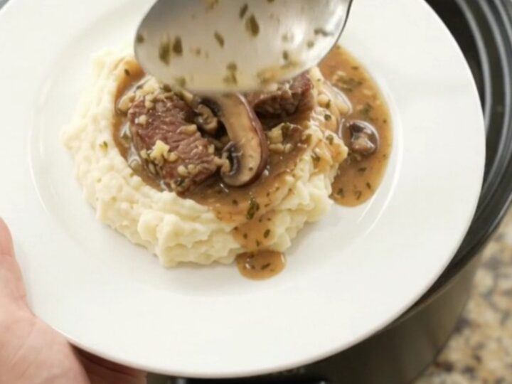Slow cooker ribeye bites and portobello mushrooms in a rich garlic-herb butter au jus, served in a black crockpot.