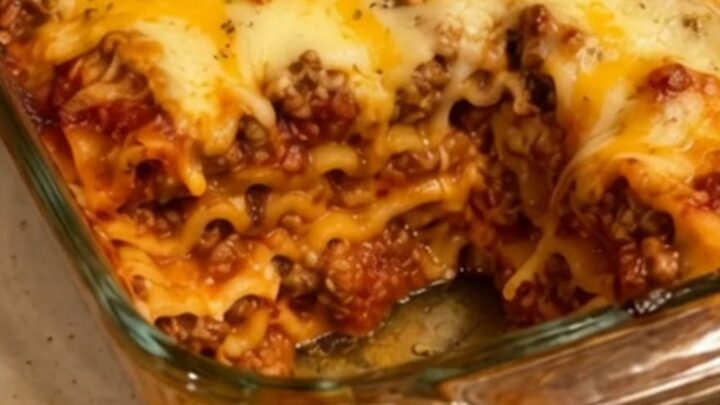 A close-up of a steaming slice of beef lasagna being lifted from a glass dish with a perfect cheese pull.