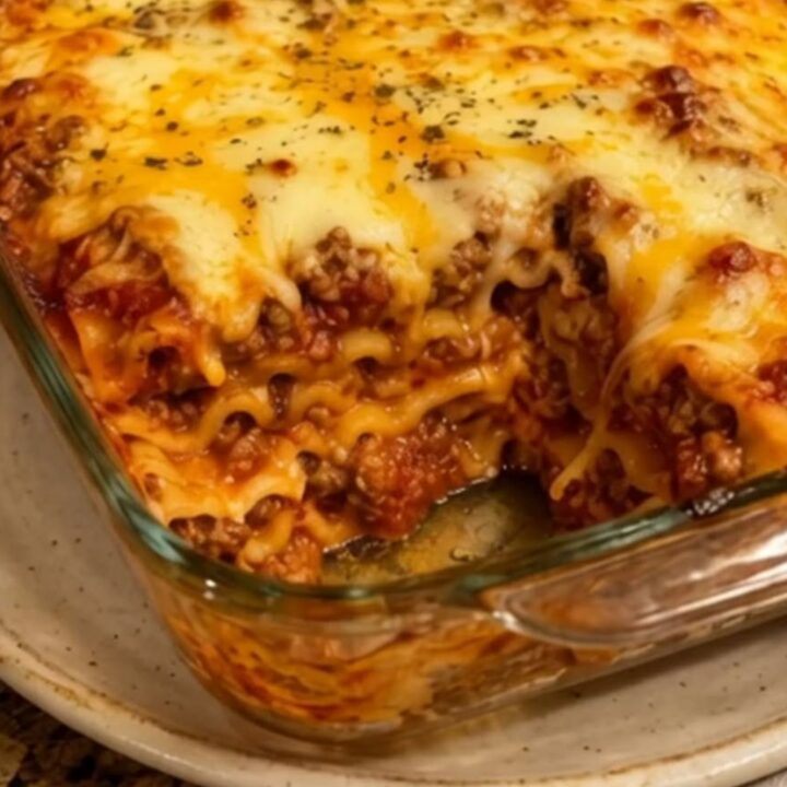 A close-up of a steaming slice of beef lasagna being lifted from a glass dish with a perfect cheese pull.