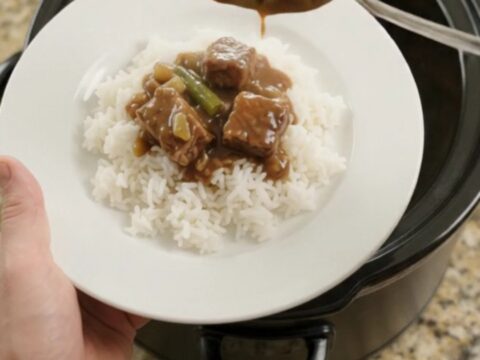 Slow cooker with tender ribeye bites, green beans, and potatoes in bourbon gravy