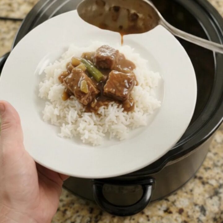 Slow cooker with tender ribeye bites, green beans, and potatoes in bourbon gravy