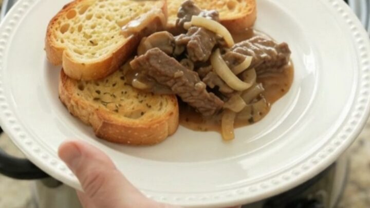 Slow cooker flank steak in creamy Gruyère mushroom sauce, bubbling in a black Crockpot