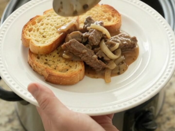 Slow cooker flank steak in creamy Gruyère mushroom sauce, bubbling in a black Crockpot