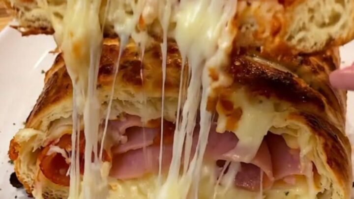 A golden, crusty pizza stromboli sliced open to reveal melted mozzarella, pepperoni, and ham.