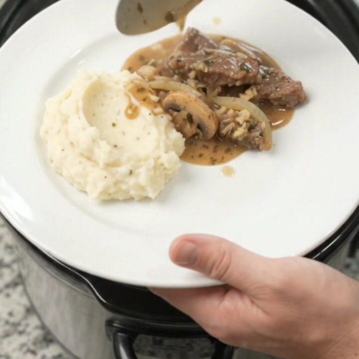 Cowboy butter mushroom flank steak in a slow cooker, bubbling in rich gravy