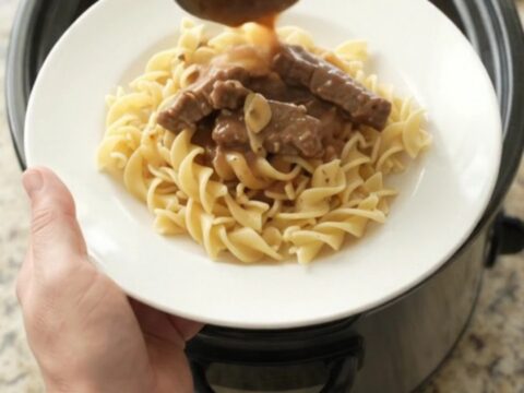 Slow cooker flank steak and baby potatoes in a rich sour cream gravy, served on a white plate