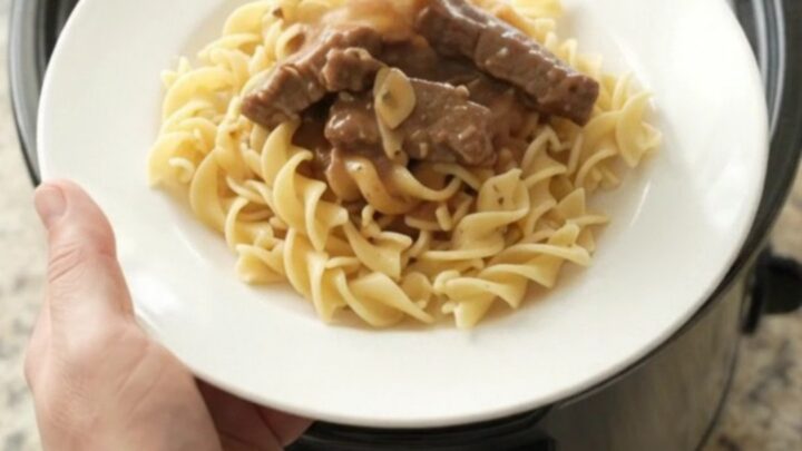 Slow cooker flank steak and baby potatoes in a rich sour cream gravy, served on a white plate