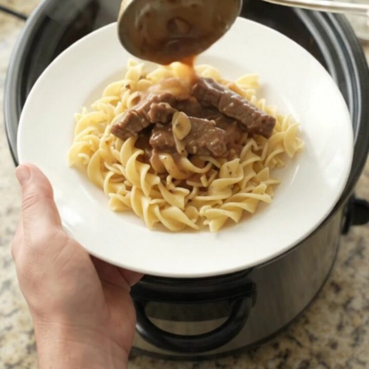 Slow cooker flank steak and baby potatoes in a rich sour cream gravy, served on a white plate