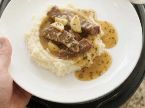 Slow cooker filled with tender flank steak, baby potatoes, and garlic herb butter au jus, bubbling and steaming.