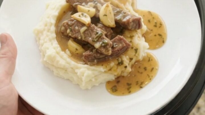 Slow cooker filled with tender flank steak, baby potatoes, and garlic herb butter au jus, bubbling and steaming.