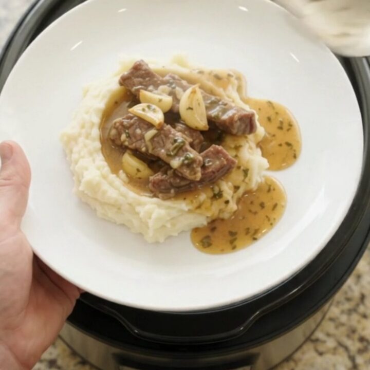 Slow cooker filled with tender flank steak, baby potatoes, and garlic herb butter au jus, bubbling and steaming.