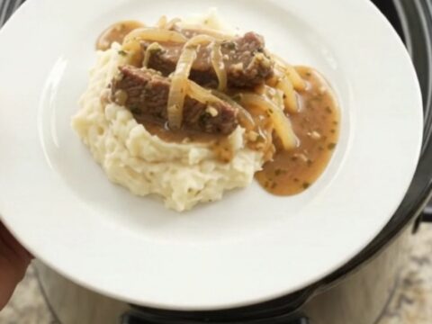Slow cooker flank steak with onions in buttery au jus, topped with melted butter