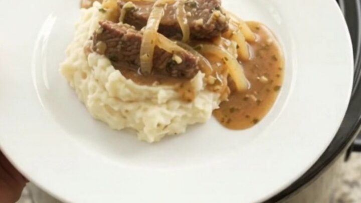 Slow cooker flank steak with onions in buttery au jus, topped with melted butter