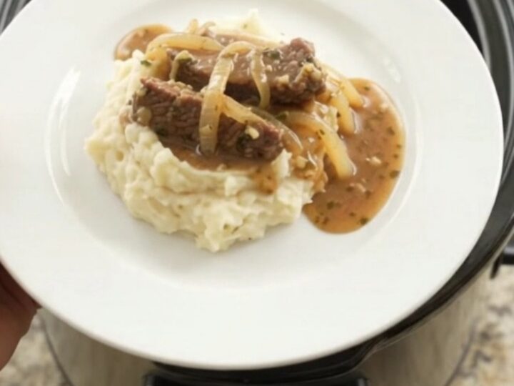 Slow cooker flank steak with onions in buttery au jus, topped with melted butter