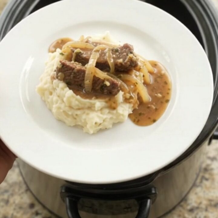 Slow cooker flank steak with onions in buttery au jus, topped with melted butter