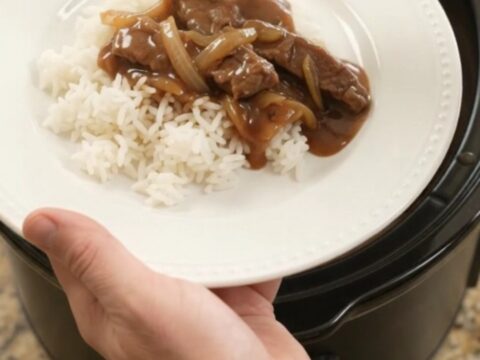 Slow cooker filled with tender beef strips and caramelized onions in rich bourbon gravy