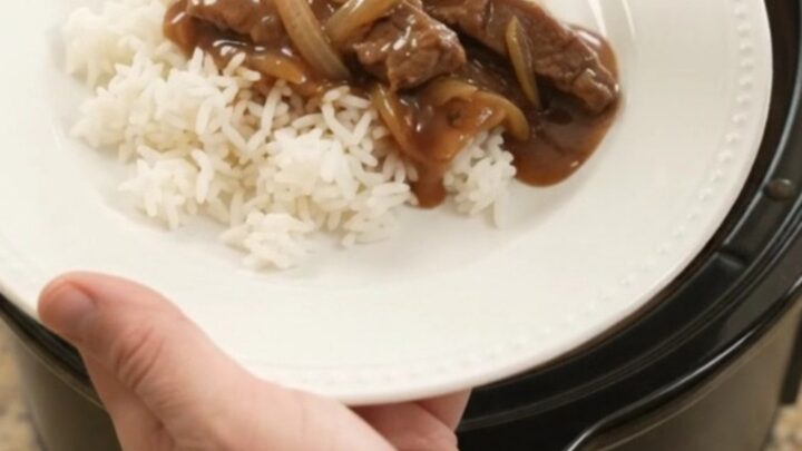 Slow cooker filled with tender beef strips and caramelized onions in rich bourbon gravy