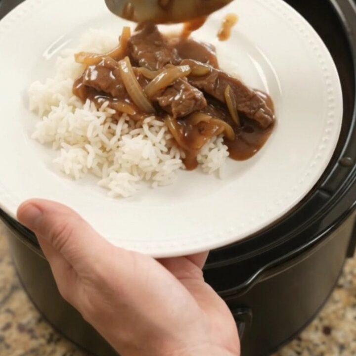 Slow cooker filled with tender beef strips and caramelized onions in rich bourbon gravy
