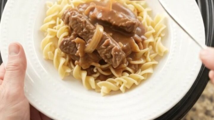 Slow cooker flank steak with sour cream gravy, peppers, and onions in a black crockpot