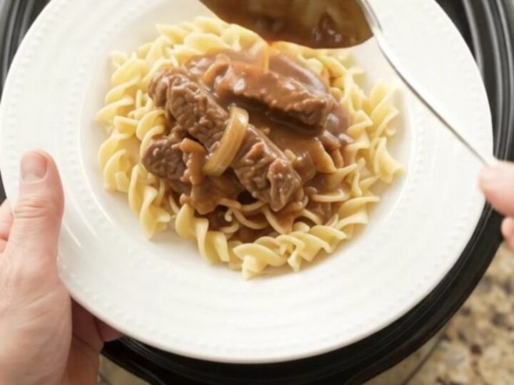 Slow cooker flank steak with sour cream gravy, peppers, and onions in a black crockpot