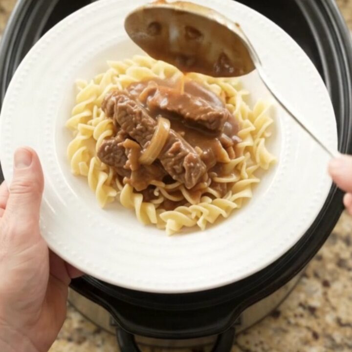 Slow cooker flank steak with sour cream gravy, peppers, and onions in a black crockpot