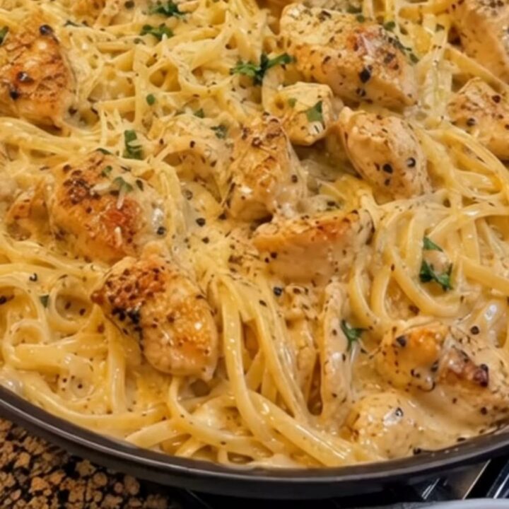 A close-up view of creamy linguine with seared chicken pieces in a skillet.
