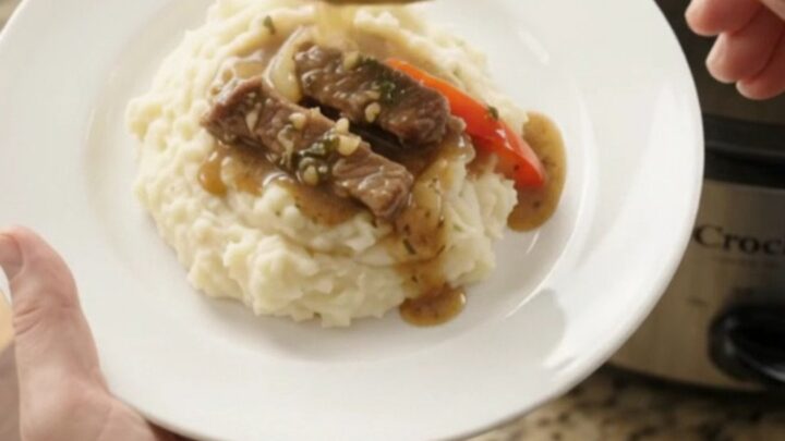 Slow-cooker cowboy butter flank steak with bell peppers and red onions in a rich au jus, served on a white plate.