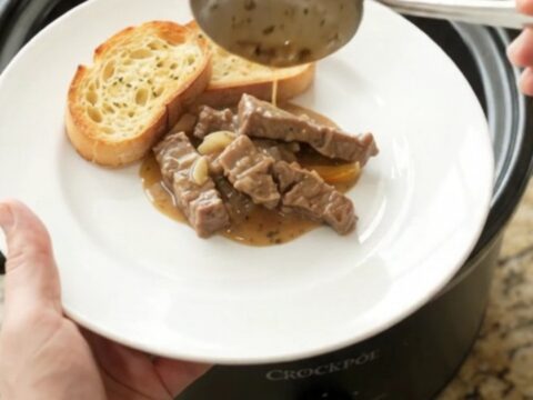 A slow cooker filled with creamy flank steak, peppers, and onions in a rich Gruyère sauce.