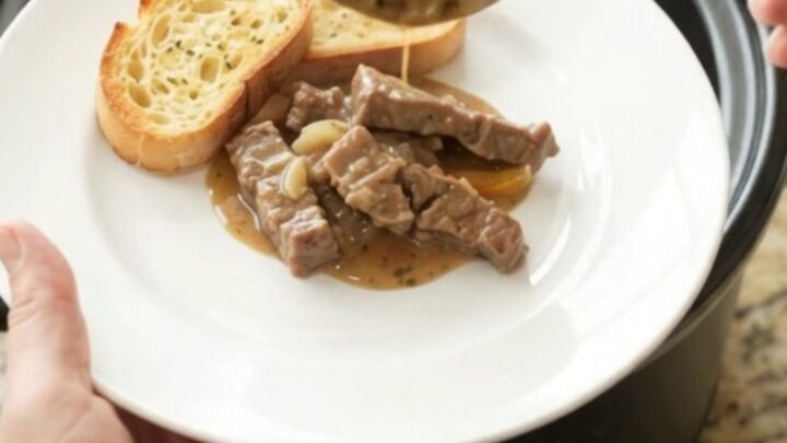 A slow cooker filled with creamy flank steak, peppers, and onions in a rich Gruyère sauce.