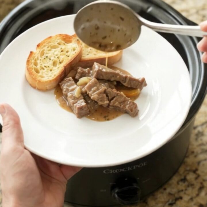 A slow cooker filled with creamy flank steak, peppers, and onions in a rich Gruyère sauce.