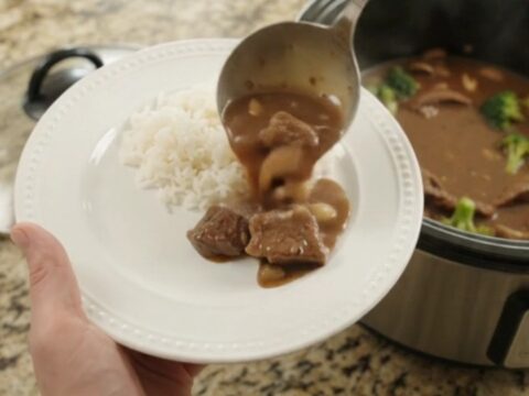 Slow cooker full of tender flank steak, broccoli, and mushrooms in glossy bourbon gravy